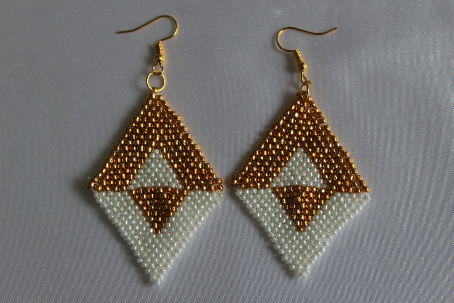 Handmade gold and white diamond-shaped seed bead earrings featuring a geometric woven design with gold-tone fish hook ear wires, lightweight boho statement jewellery.