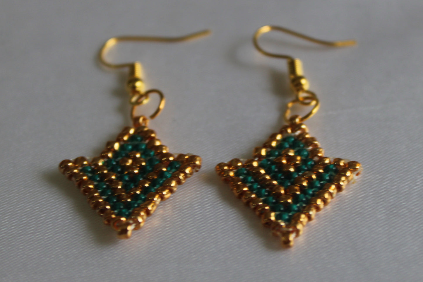 Handmade emerald green and gold seed bead earrings featuring a geometric star-inspired design with gold-tone fish hook ear wires, lightweight boho statement jewellery.