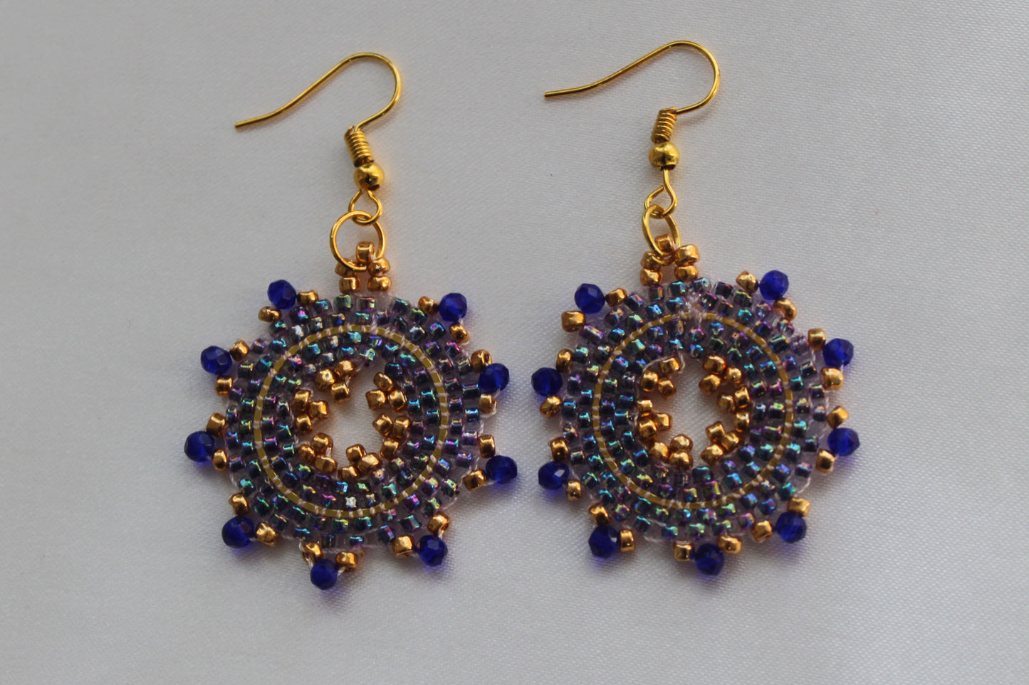 Handmade blue and gold sunburst beaded earrings featuring a circular mandala-inspired seed bead design with gold-tone fish hook ear wires, lightweight boho statement jewellery.