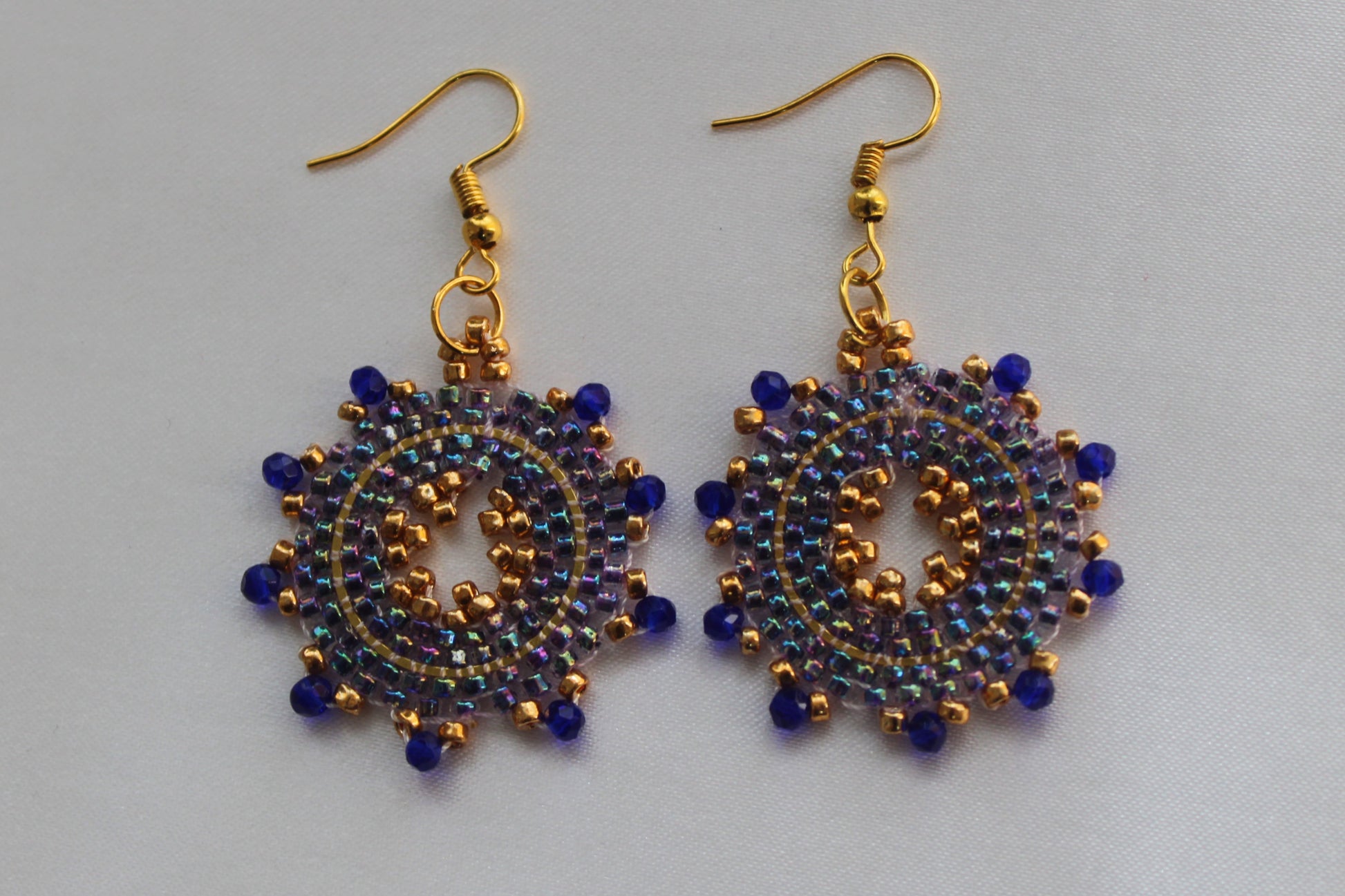 Handmade blue and gold sunburst beaded earrings featuring a circular mandala-inspired seed bead design with gold-tone fish hook ear wires, lightweight boho statement jewellery.