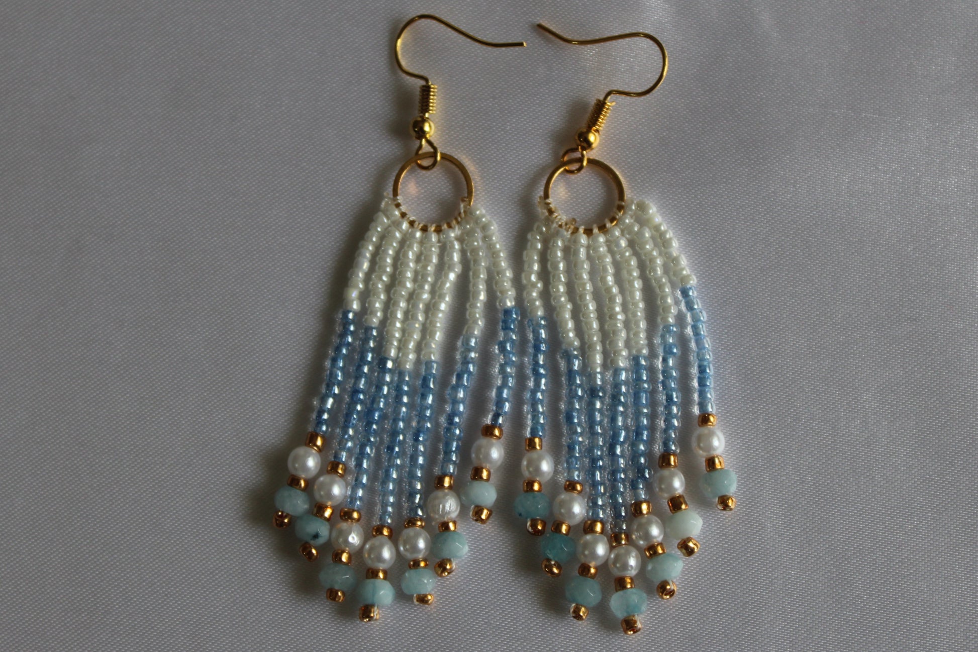 Handmade white and sky-blue beaded fringe earrings with pearl accents, cascading tassel design, gold-tone hoop connectors, and fish hook ear wires, lightweight boho dangle jewellery.