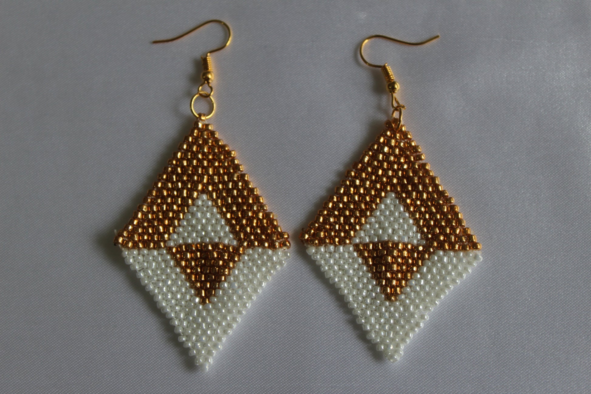 Handmade gold and white diamond-shaped seed bead earrings featuring a geometric woven design with gold-tone fish hook ear wires, lightweight boho statement jewellery.