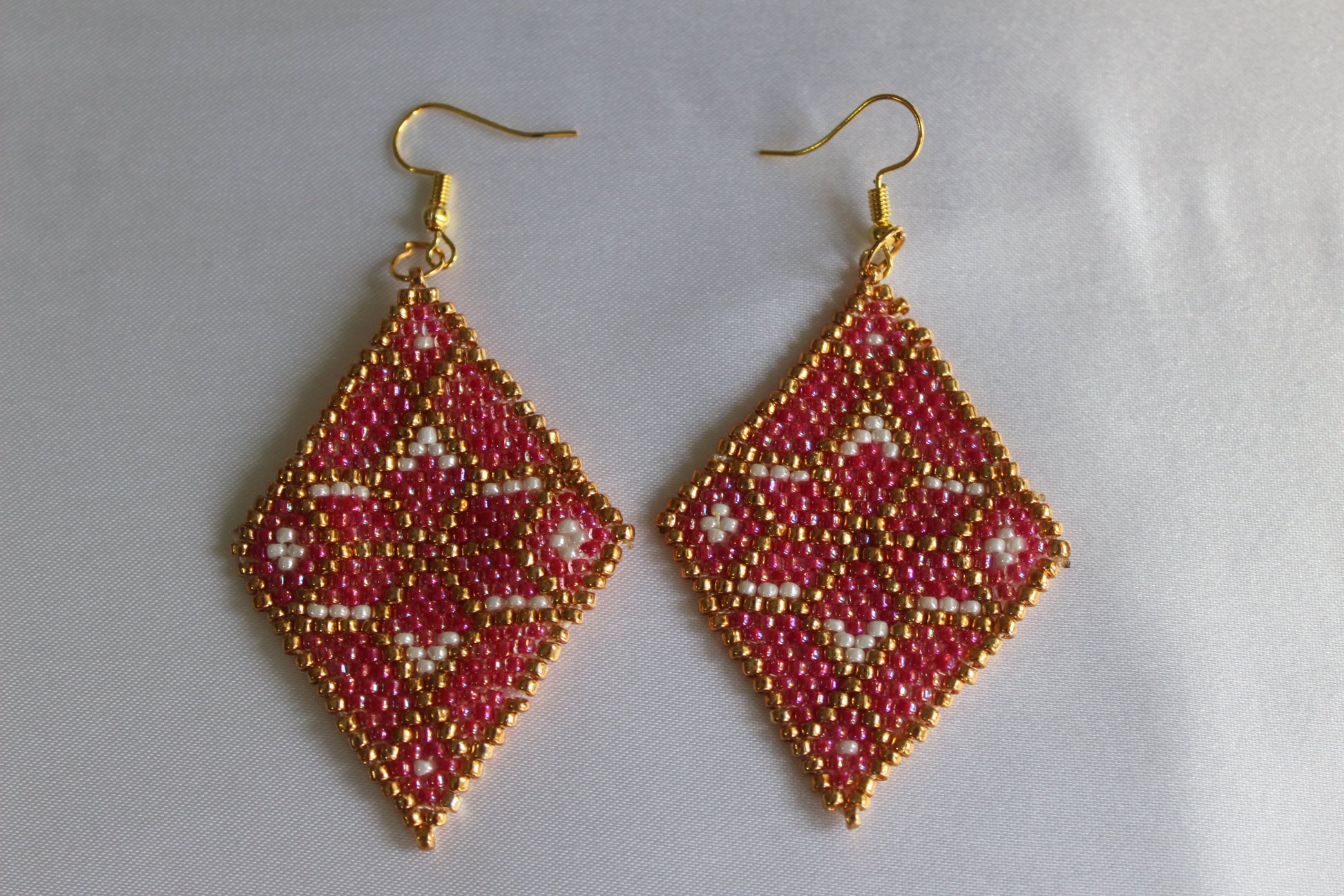 Handmade diamond-shaped seed bead earrings in pink, gold, and white featuring a geometric woven design with gold-tone fish hook ear wires, lightweight boho statement jewellery.