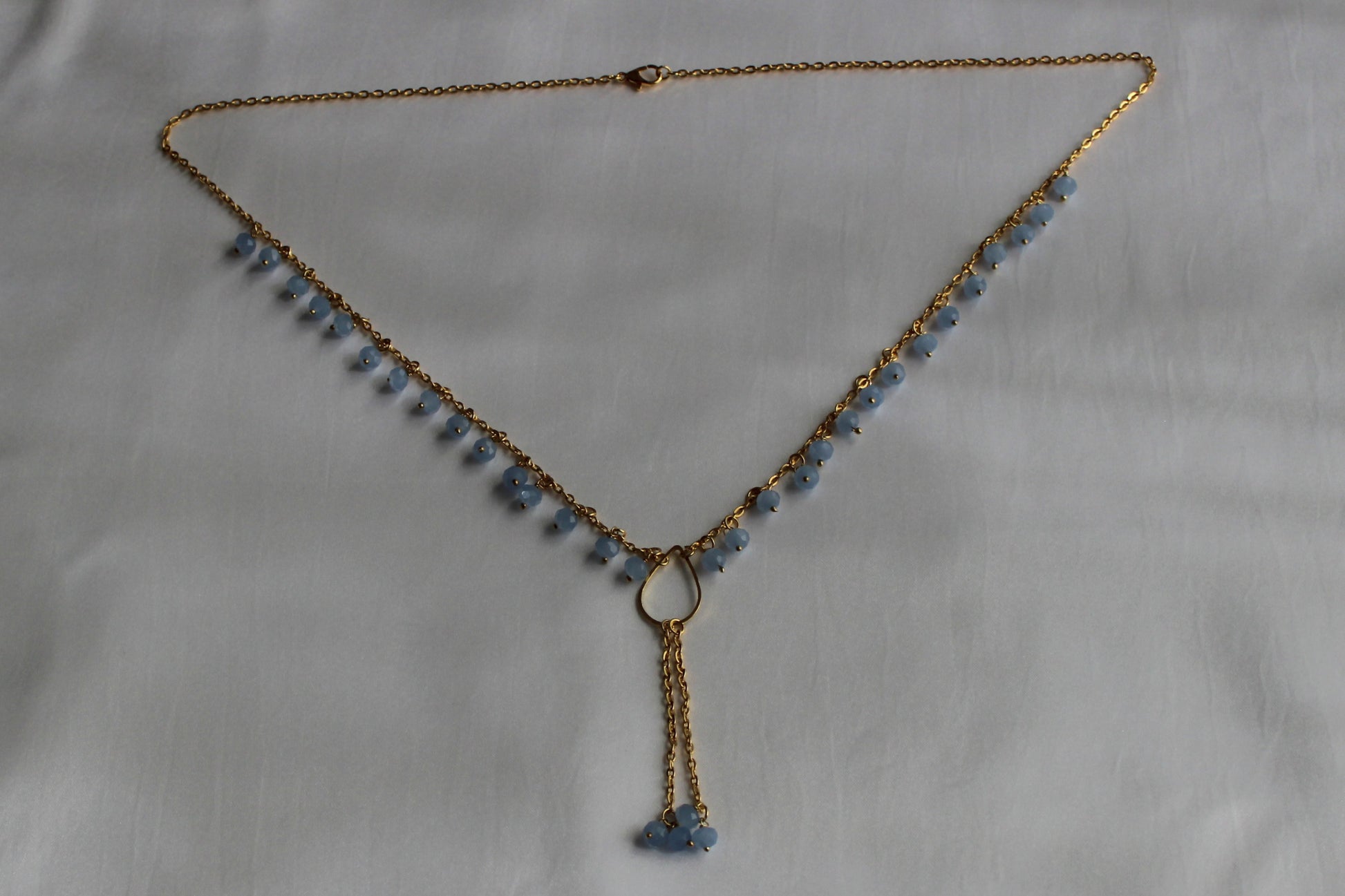 Handmade sky blue beaded Y necklace with gold-tone chain and elegant lariat drop pendant displayed on a white background.