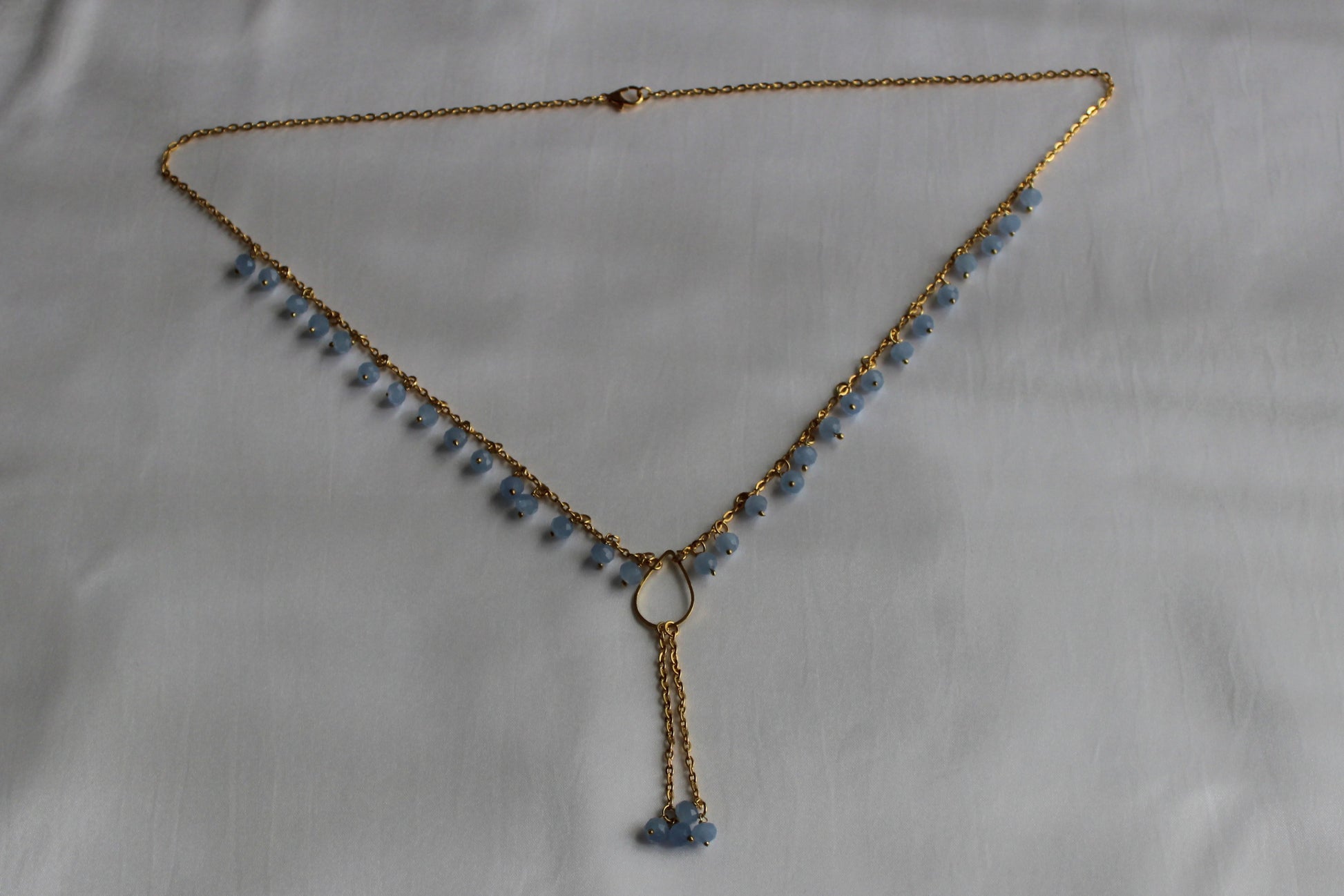 Handmade sky blue beaded Y necklace with gold-tone chain and elegant lariat drop pendant displayed on a white background.