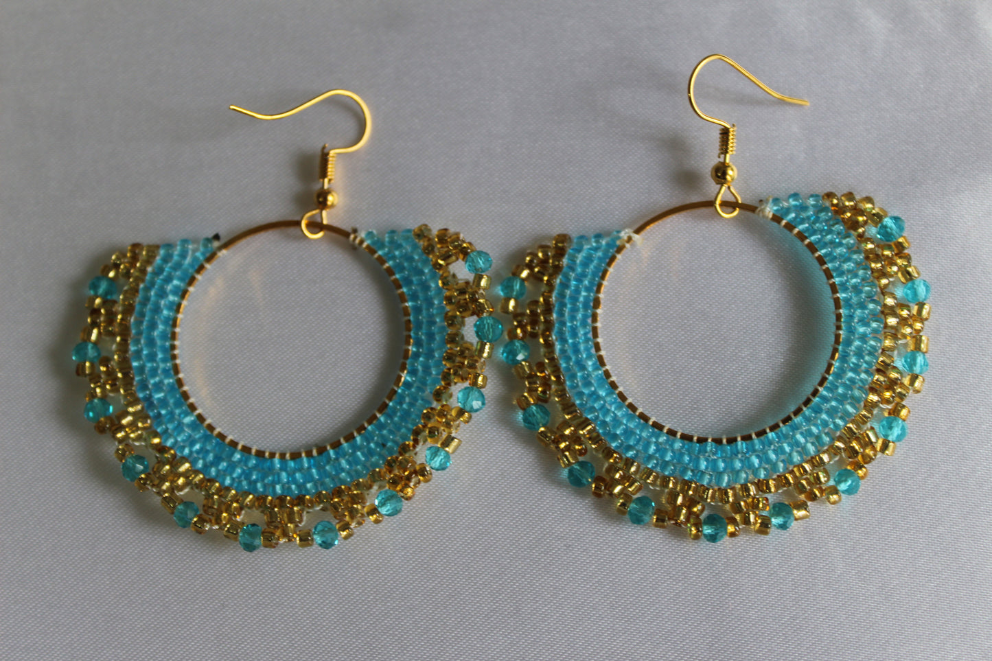 Handmade turquoise blue and gold beaded hoop earrings featuring intricate seed bead embroidery on gold-tone hoops with fish hook ear wires, lightweight boho statement jewellery.