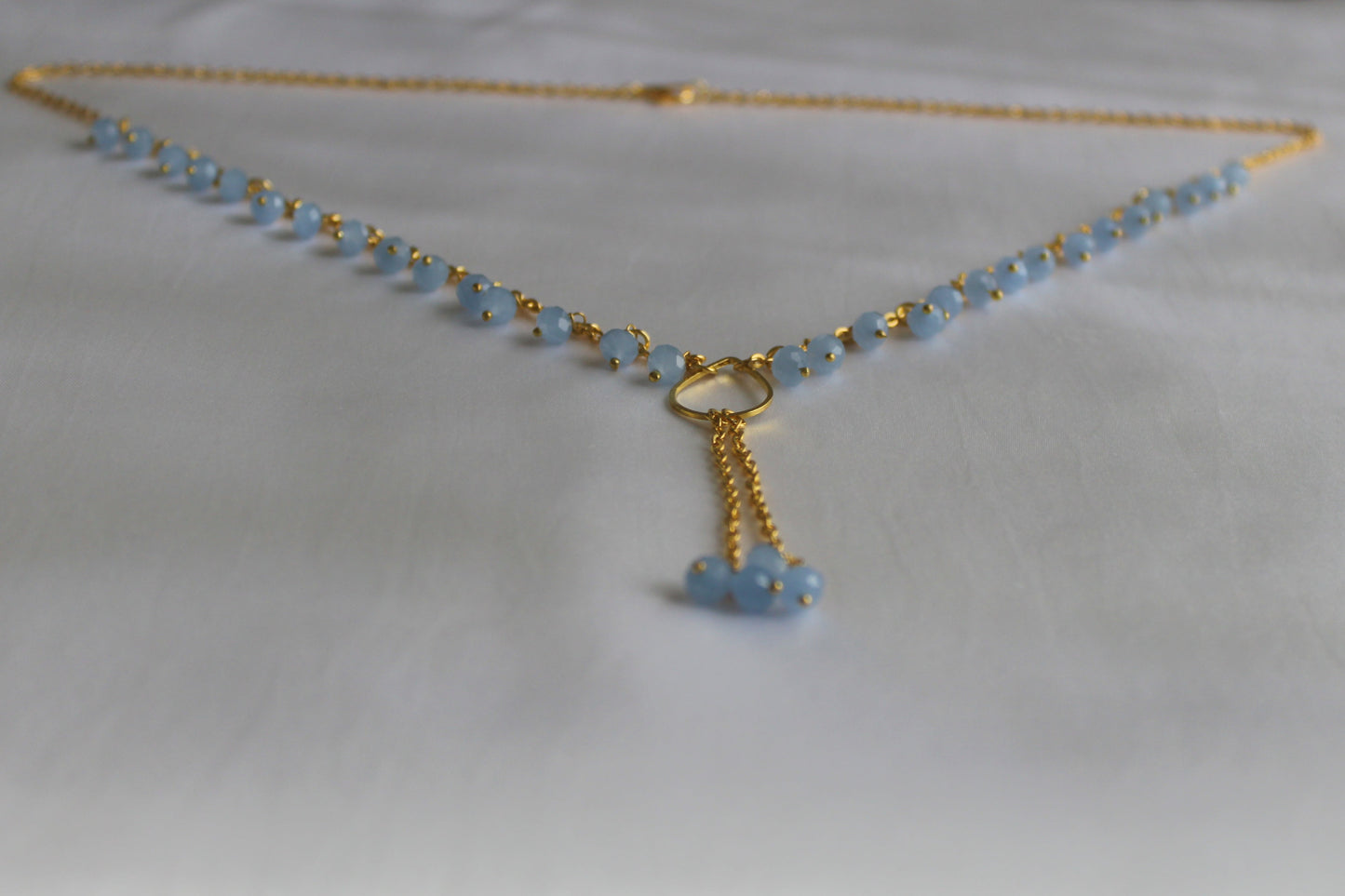 Handmade sky blue beaded Y necklace with gold-tone chain and elegant lariat drop pendant displayed on a white background.